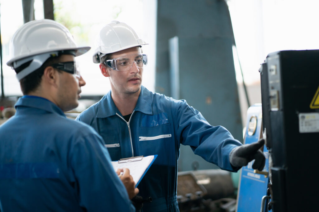 Two factory workers in hardhats examining a piece of machinery 